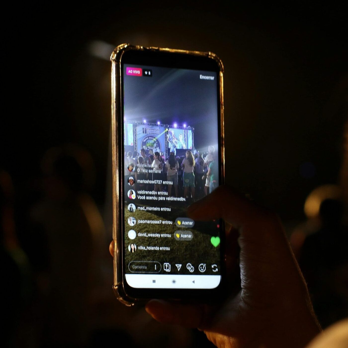 A woman live streams a concert using her smartphone at night. Vibrant stage in view.