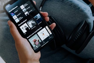 Close-up of a person holding a smartphone with headphones, browsing a music app.